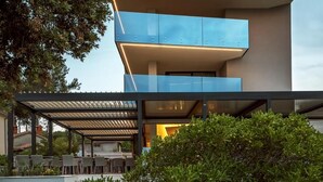 Una casa moderna de dos pisos con techo plano, ventanas amplias y un espacio cubierto para sentarse al aire libre.