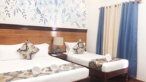 A hotel room with two beds, a wooden headboard, a nightstand with a lamp, and a window with blue curtains. - Blue Waters Inn Coron (Coron)