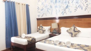 A hotel room with two beds, wooden headboards, a nightstand with a lamp, and a floral wall decoration.