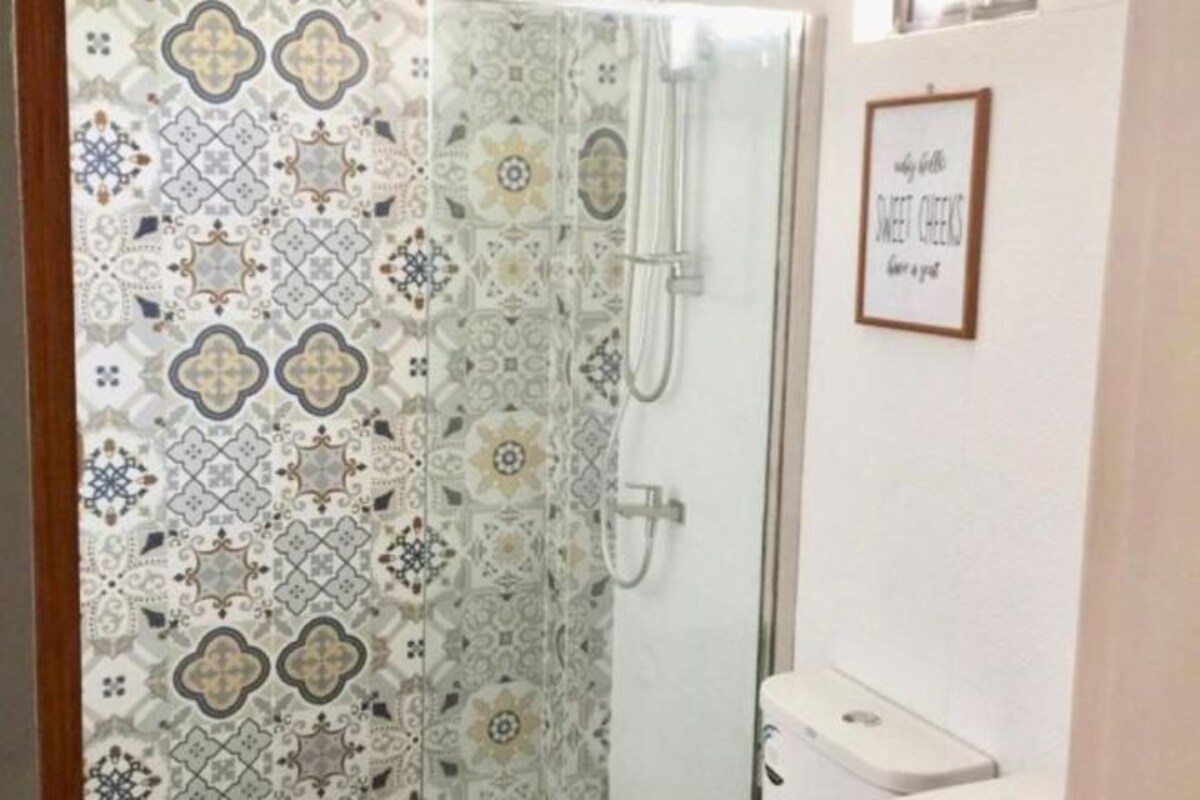 Un baño con cortina de ducha con un diseño geométrico, un cartel en la pared y un inodoro.