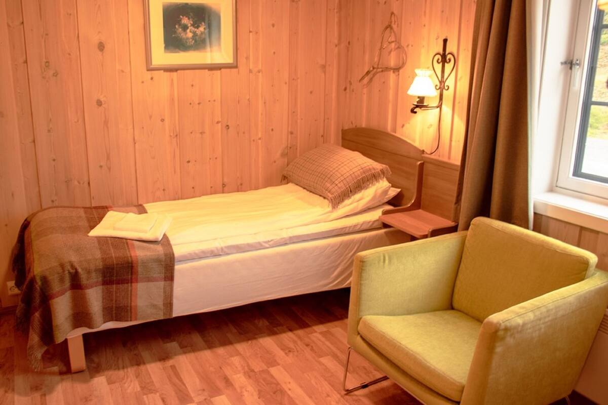 A room with a bed, a chair, a framed picture on the wall, and a window with curtains.