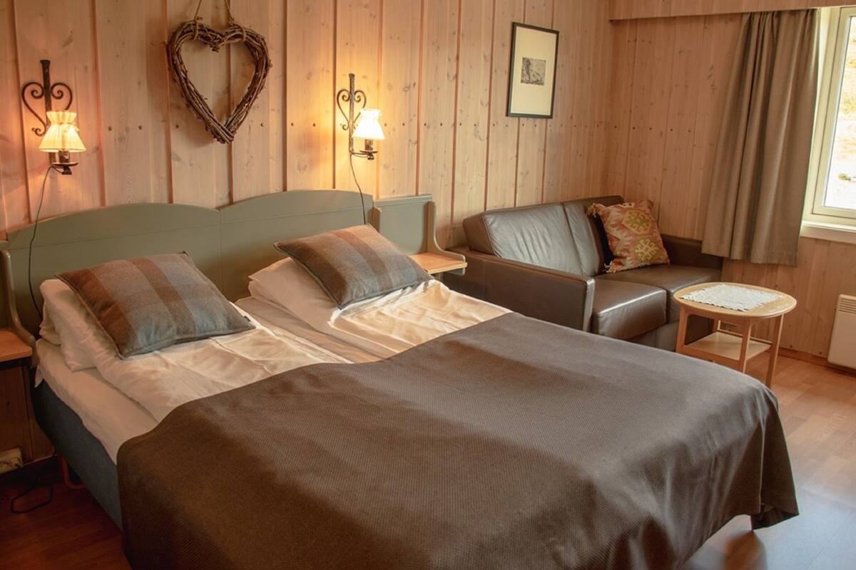 A bedroom with a bed, a sofa, a small table, and wall-mounted lamps.