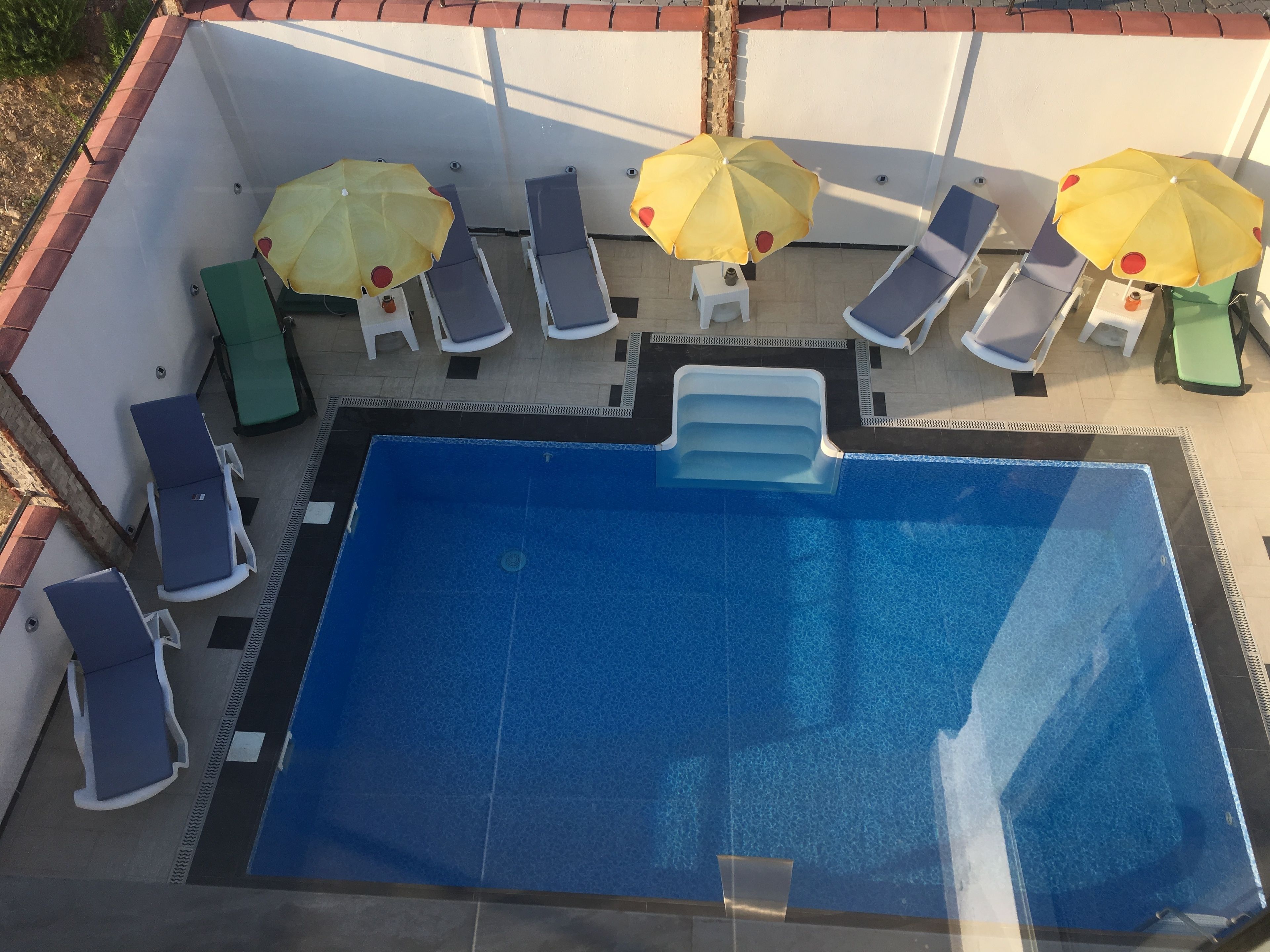 A rectangular swimming pool with a blue interior, surrounded by lounge chairs and yellow umbrellas.