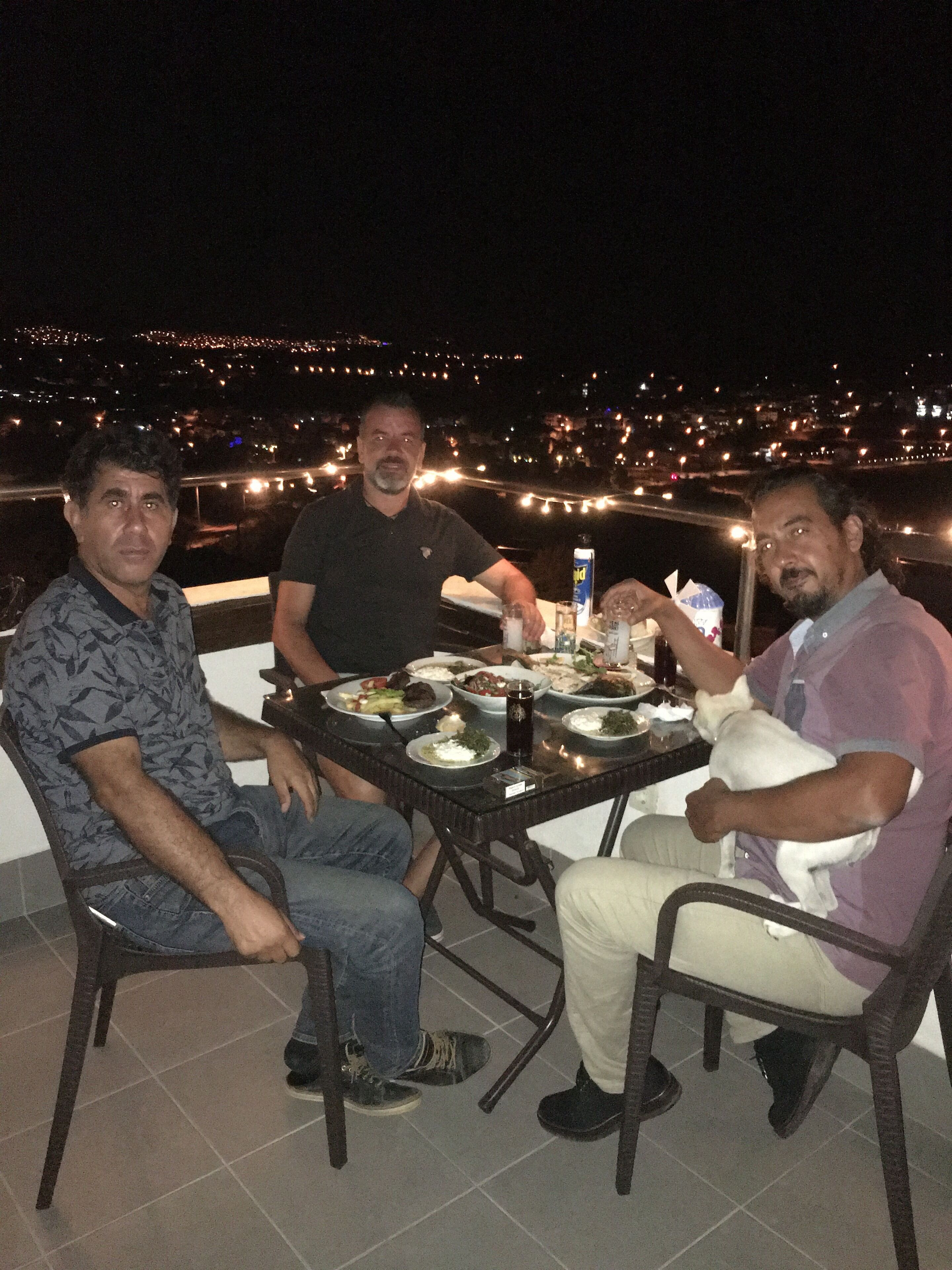 Three people seated at an outdoor table with a city view in the background.