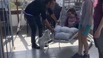 Een overdekt buitengebied met uitzicht op verre bergen, een hangstoel en een persoon die met een hond bezig is.