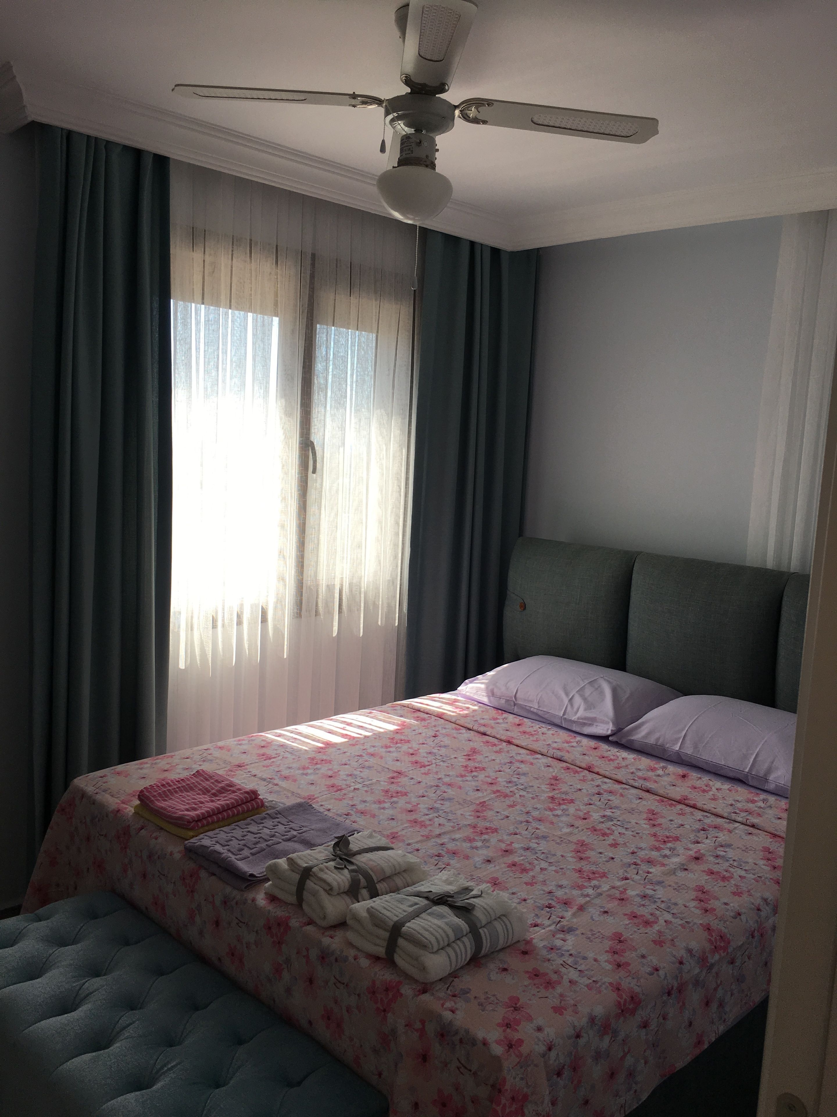 Een slaapkamer met een bed, een plafondventilator en een raam met gordijnen.