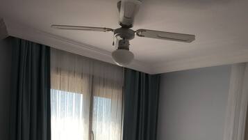 Een slaapkamer met een bed, een plafondventilator en een raam met gordijnen.