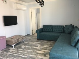 Una sala de estar con un sofá color turquesa, un mueble de madera, una cesta rosa y un televisor de pantalla plana.