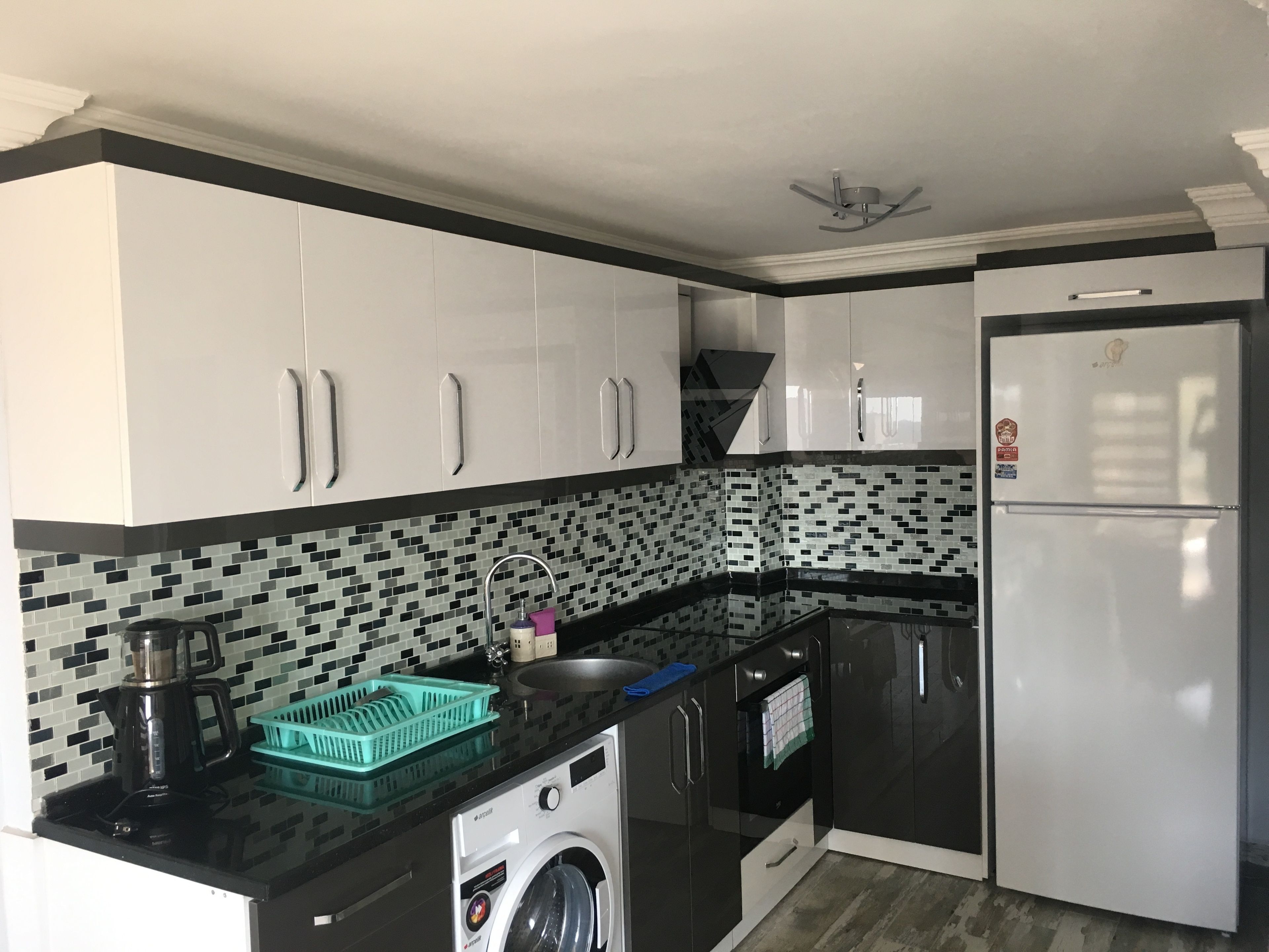 A kitchen with white cabinets, a black countertop, a washing machine, and a refrigerator.