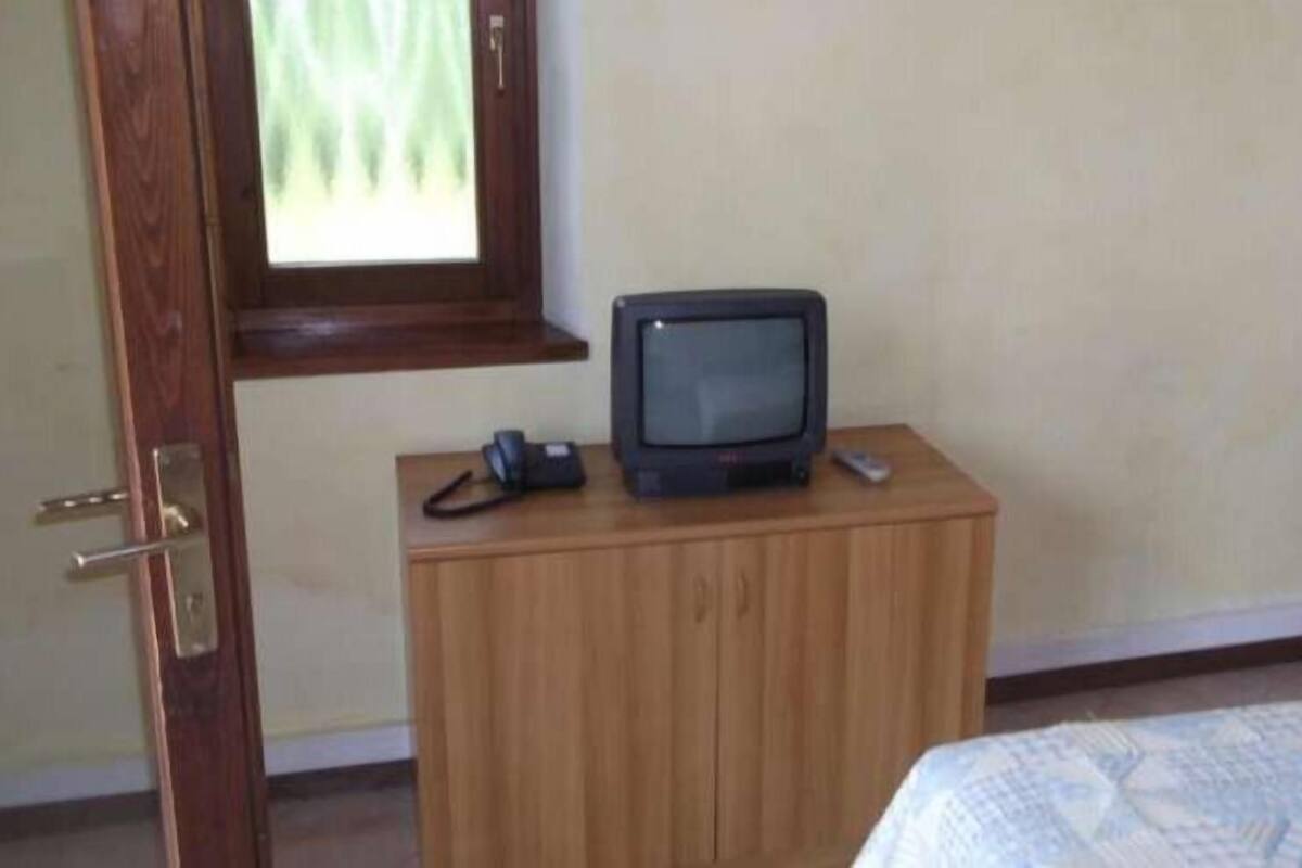 Quarto com um armário de madeira, uma televisão em cima e uma cama com manta estampada.