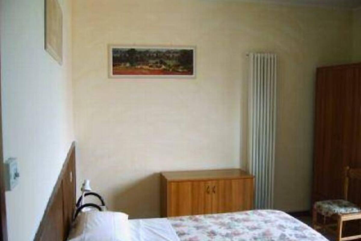 Quarto com cama, armário de madeira, radiador e uma cadeira.