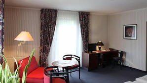 A hotel room with a bed, a desk with a lamp, a chair, a small table, and a plant. - Hotel Buchholz (Berlin)
