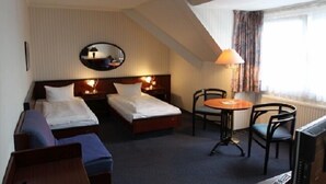 A hotel room with two single beds, a small table with chairs, a TV, and a window with curtains. - Hotel Buchholz (Berlin)