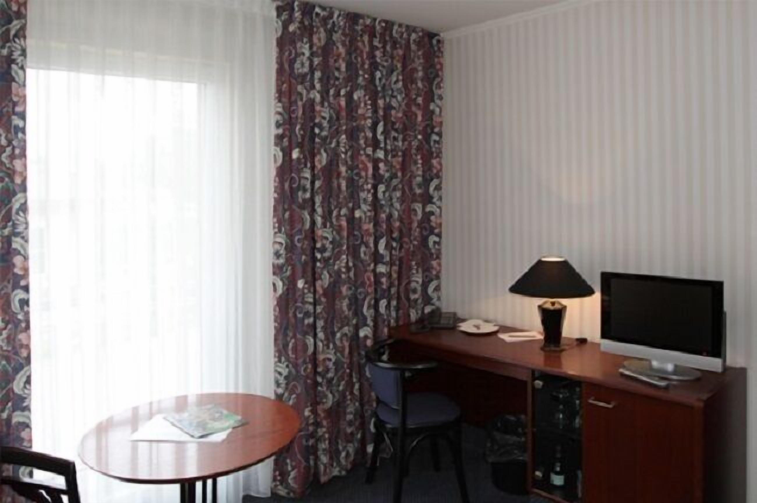 A hotel room with a desk, a chair, a television, and a lamp.