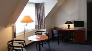 A small, compact room with a sloped ceiling, a desk with a computer, a chair, a small table, and a lamp. - Hotel Buchholz (Berlin)