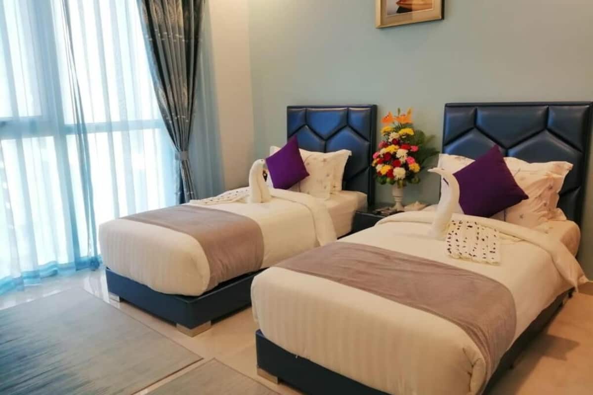 Two beds with headboards, a nightstand with a vase of flowers, and a window with sheer curtains.