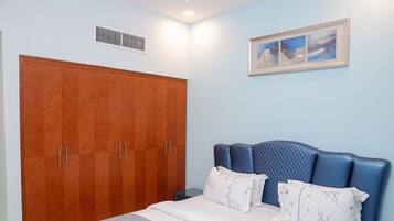 A bedroom with a large wooden wardrobe, a bed with blue headboard, and a framed picture on the wall.