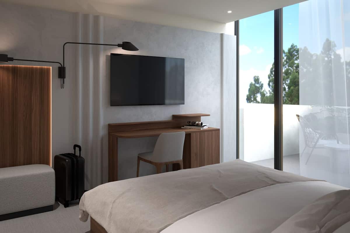 Quarto de hotel moderno com cama, escrivaninha, cadeira, televisão e mala.
