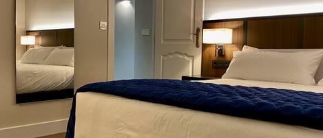 Una habitación de hotel con una cama, una mesita de noche, un espejo y una puerta.
