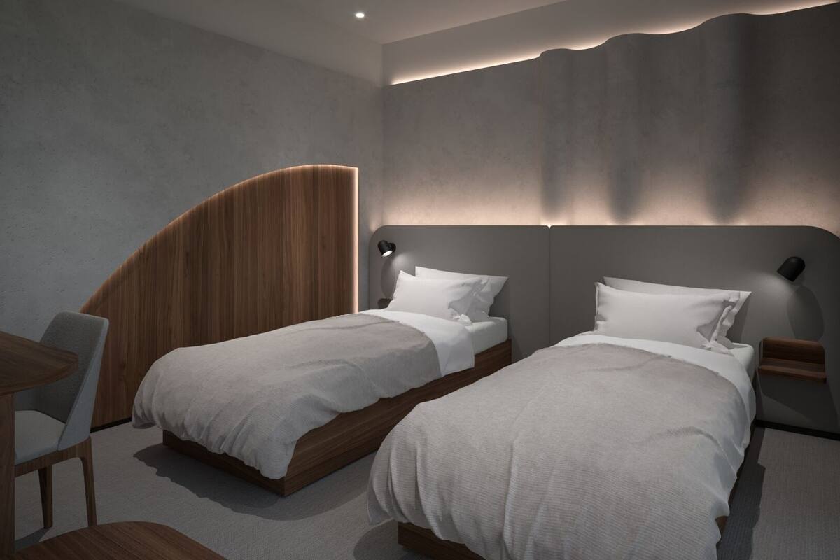 Quarto de hotel moderno com duas camas de solteiro, uma escrivaninha e uma cadeira.