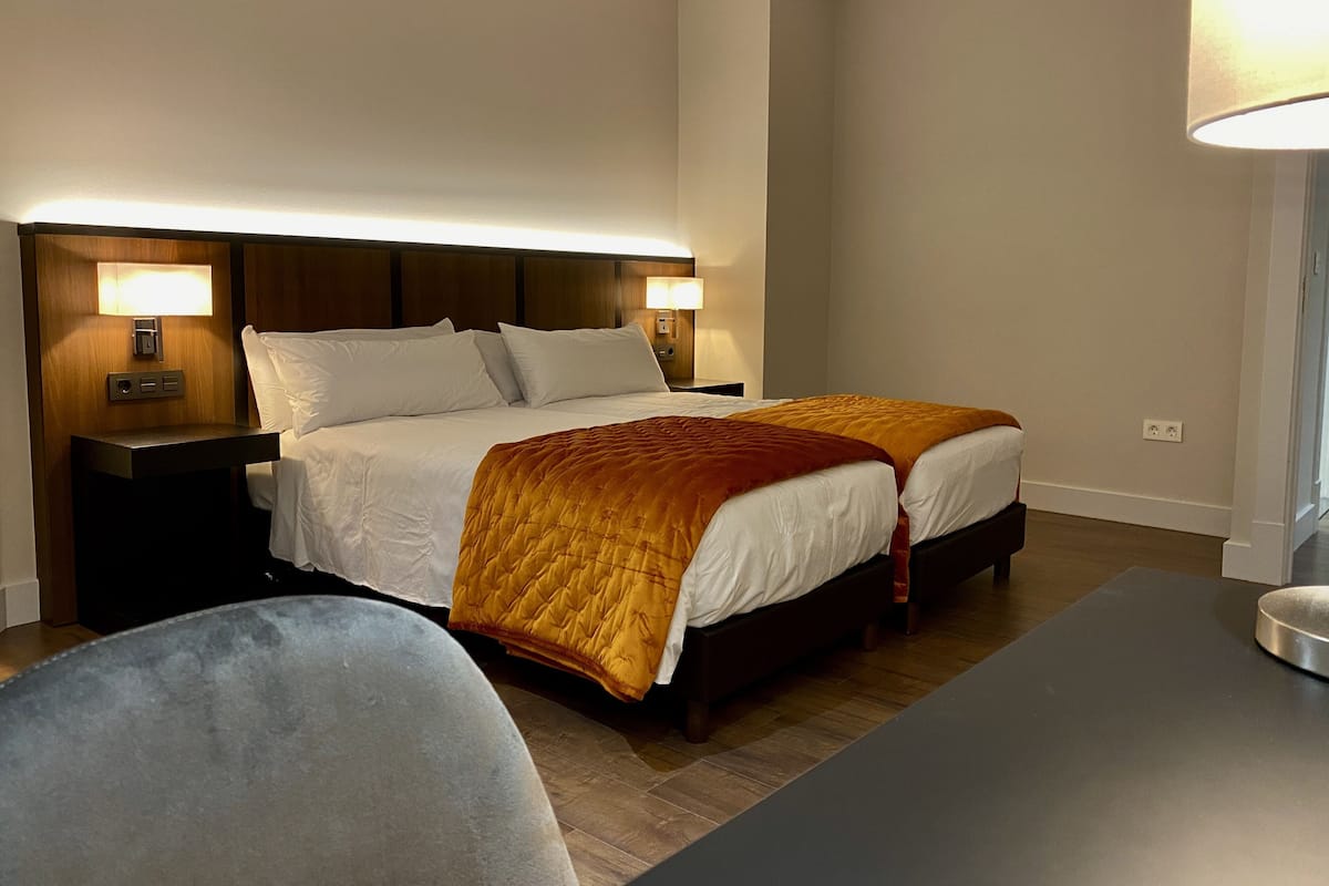 Quarto de hotel com cama de casal, duas mesas de cabeceira com luminárias, uma escrivaninha e uma cadeira.