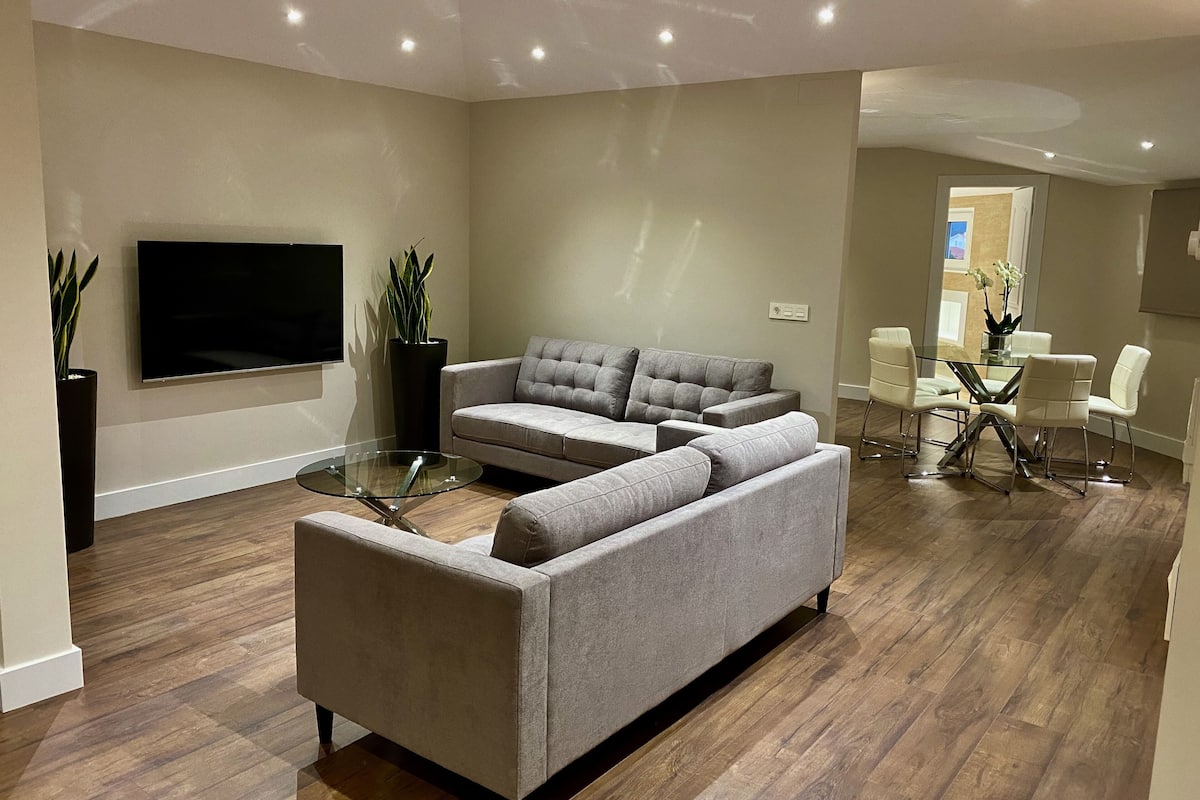 Uma sala de estar moderna com um sofá seccional, uma mesa de centro de vidro e uma televisão de tela plana na parede.