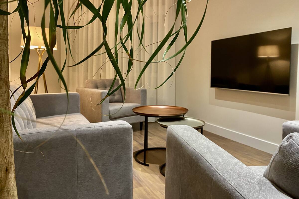 Uma sala de estar moderna com sofás cinzas, uma mesa de centro redonda e uma grande televisão de tela plana fixada na parede.