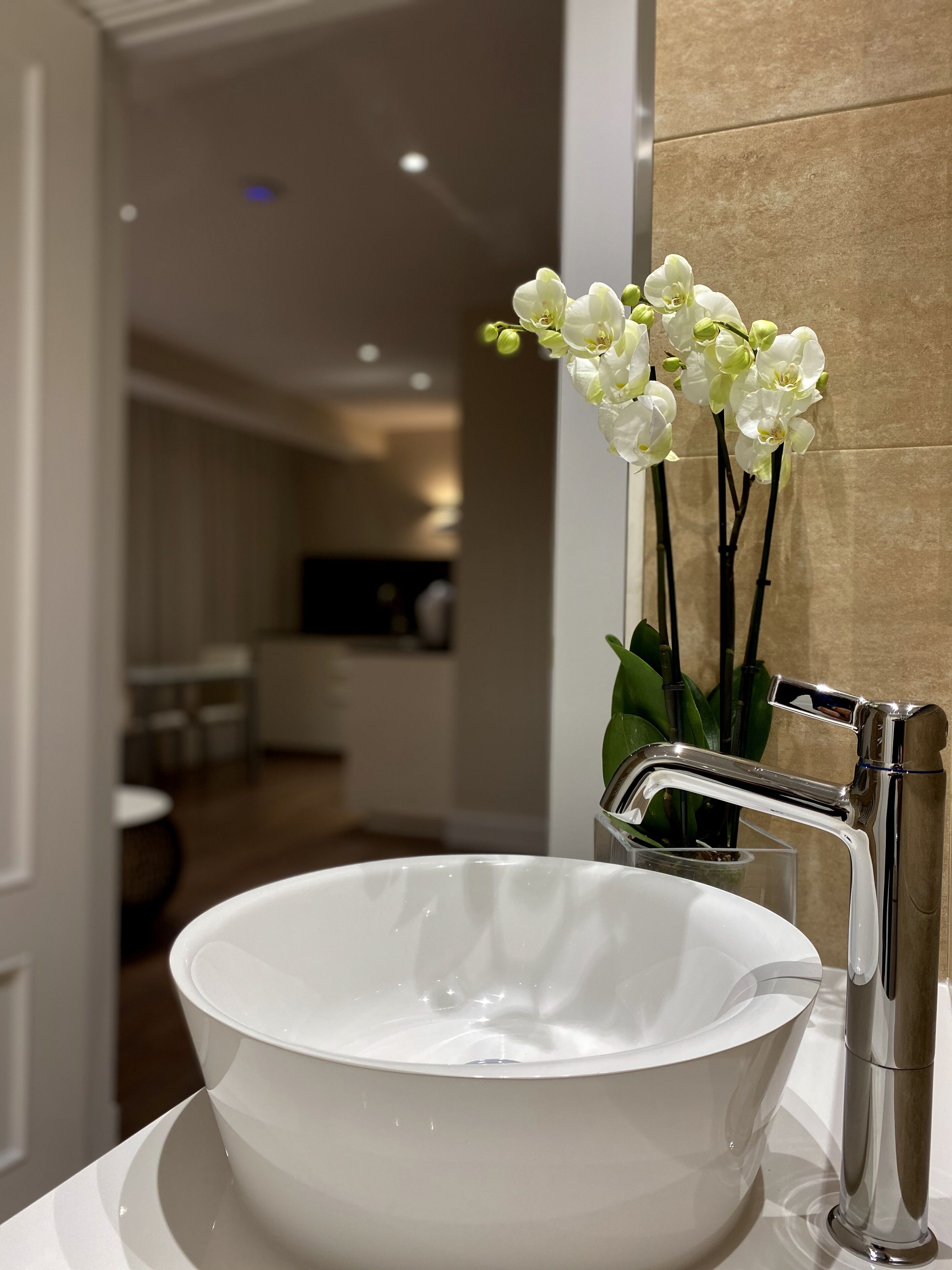 A modern bathroom with a white ceramic sink, chrome faucet, and a vase with white orchids.