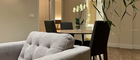 A modern living room with a grey sofa, a dining table with chairs, and a potted plant.