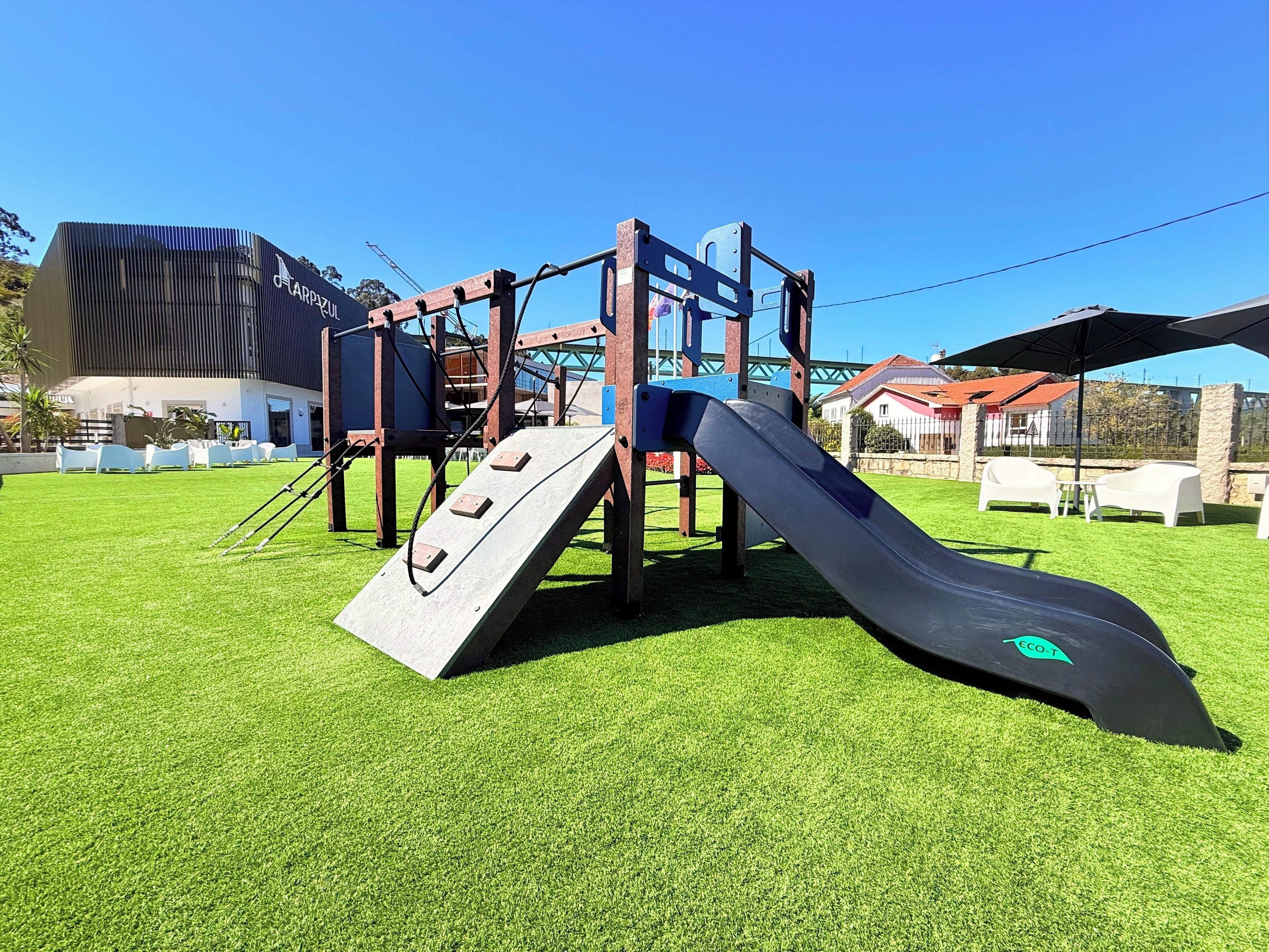 Un parque infantil con tobogán y estructura para escalar sobre césped artificial.