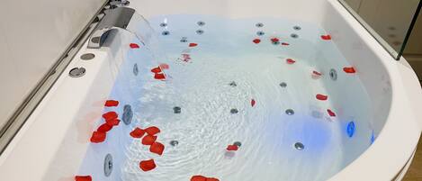 A modern spa tub with rose petals floating in the water, a control panel, and a glass enclosure.