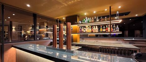 Un'area bar con un bancone in marmo, sgabelli in ottone e una selezione di bottiglie di liquori sugli scaffali.
