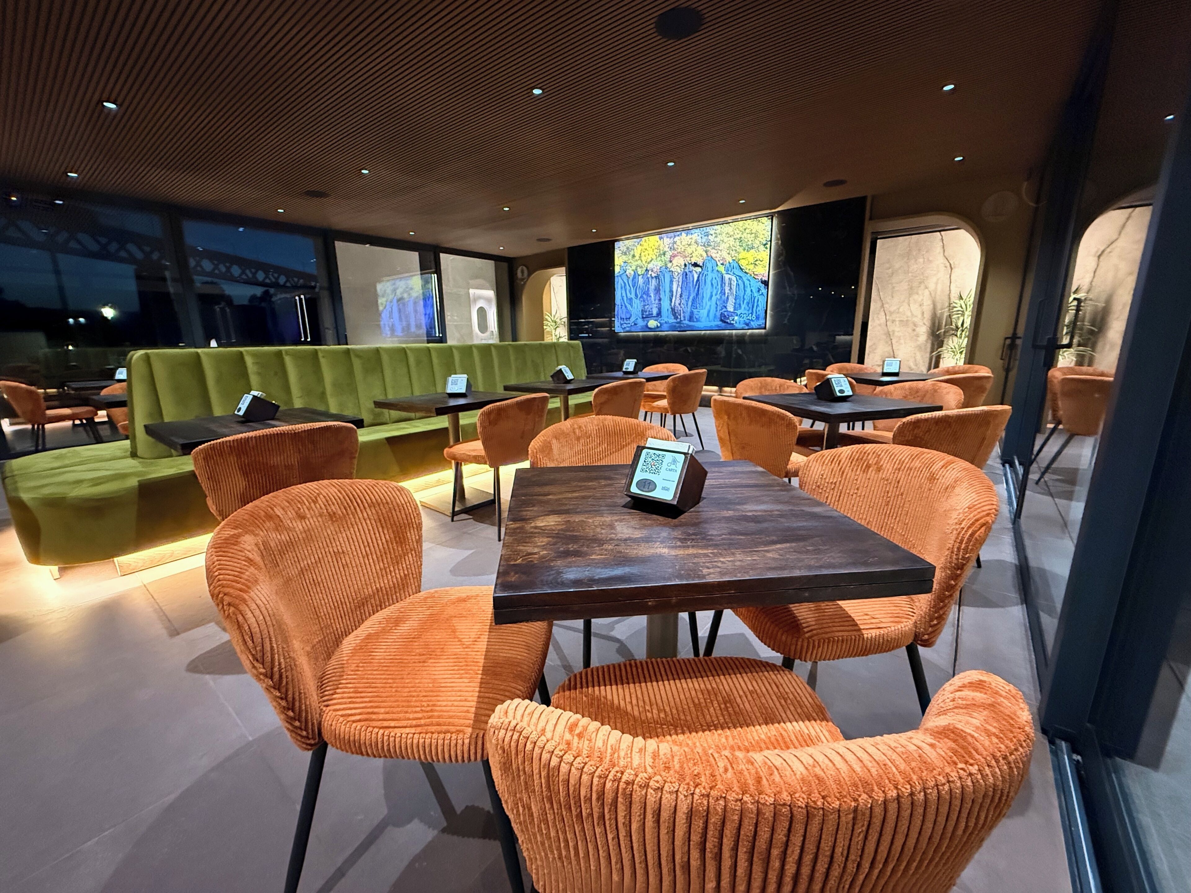Un restaurant moderne avec des chaises à revêtement orange, un canapé vert et un grand écran de télévision.