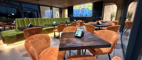 Un restaurant moderne avec des chaises à revêtement orange, un canapé vert et un grand écran de télévision.