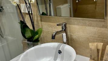 Un baño con un lavamanos blanco, un espejo y un inodoro. Hay orquídeas blancas en un jarrón sobre la encimera.