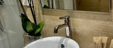 Une salle de bain avec un lavabo blanc, un miroir et des toilettes. Un vase contenant des orchidées blanches est posé sur le comptoir.