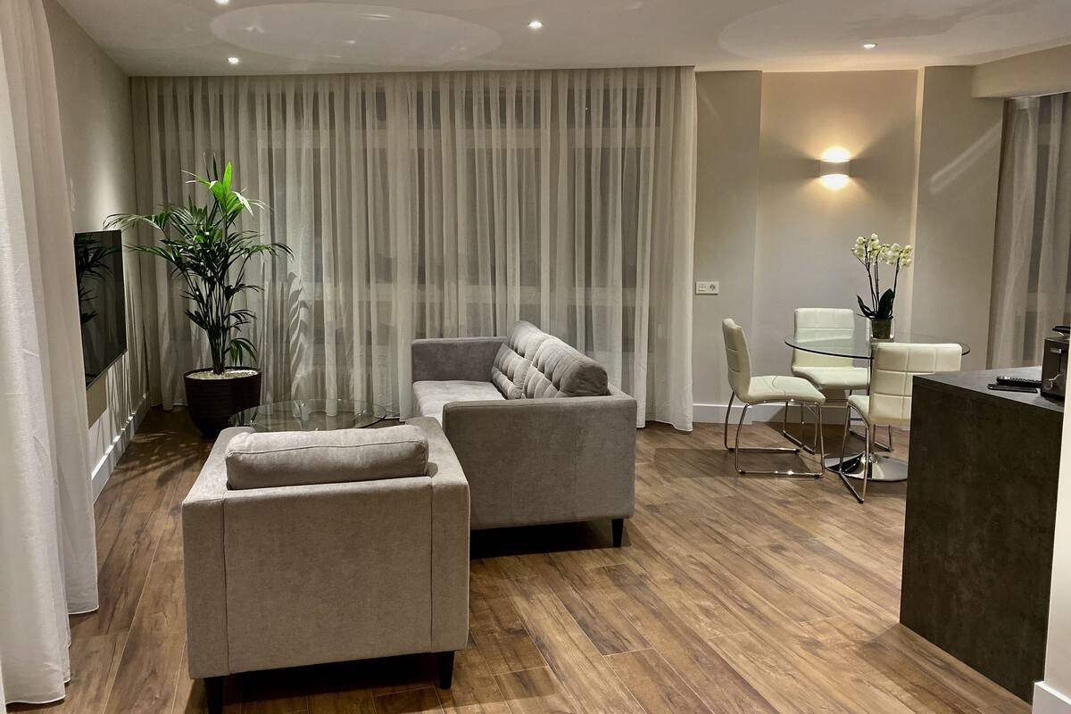 Uma sala moderna com sofá, banqueta e uma mesa de jantar de vidro com cadeiras.