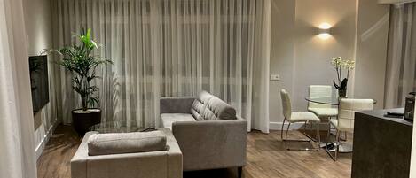 A modern living room with a sofa, ottoman, and a glass dining table with chairs.