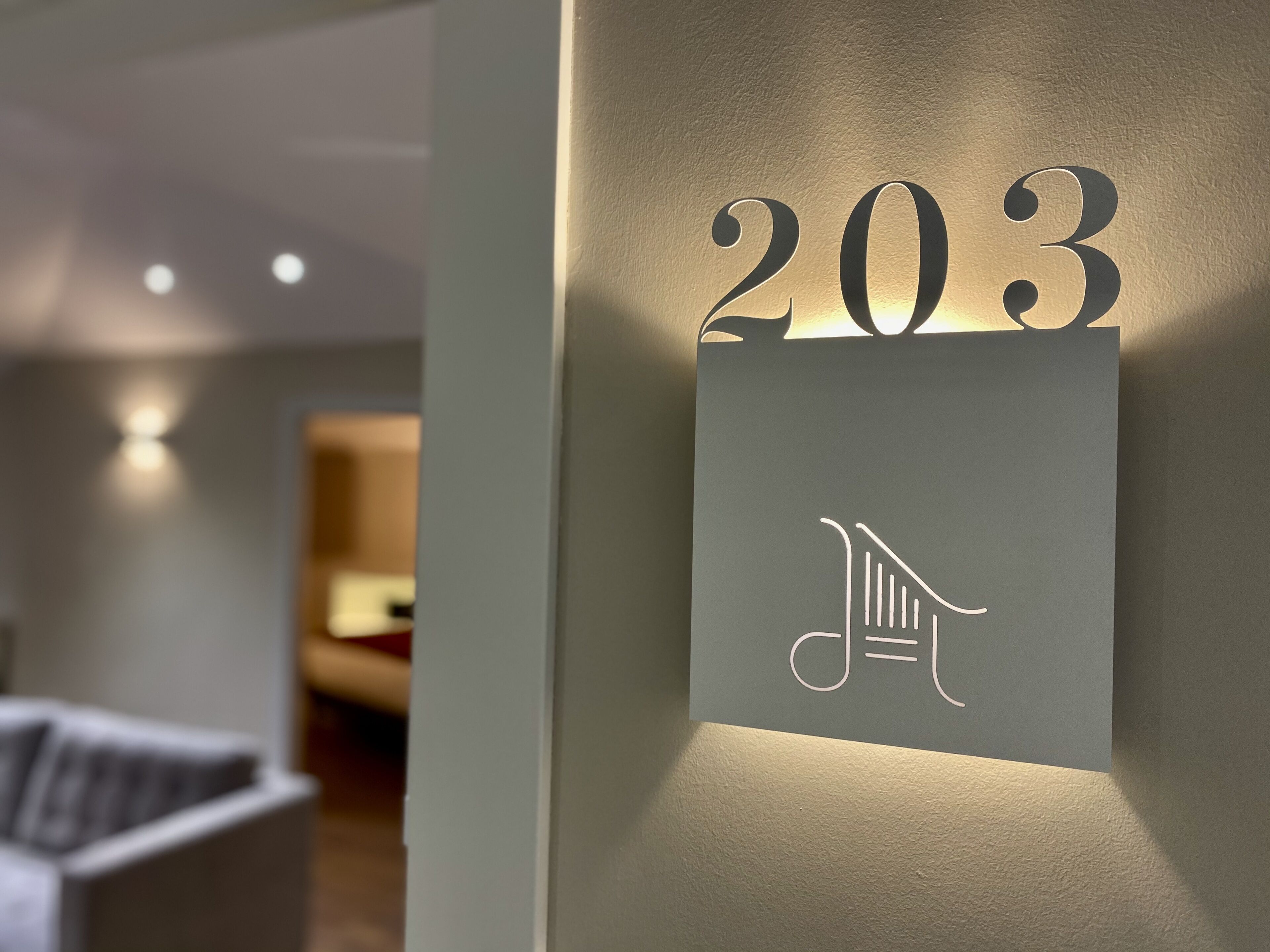Ein an der Wand befestigtes Schild mit der Nummer 203 und einem Notensymbol, das eine Hotelzimmernummer kennzeichnet.
