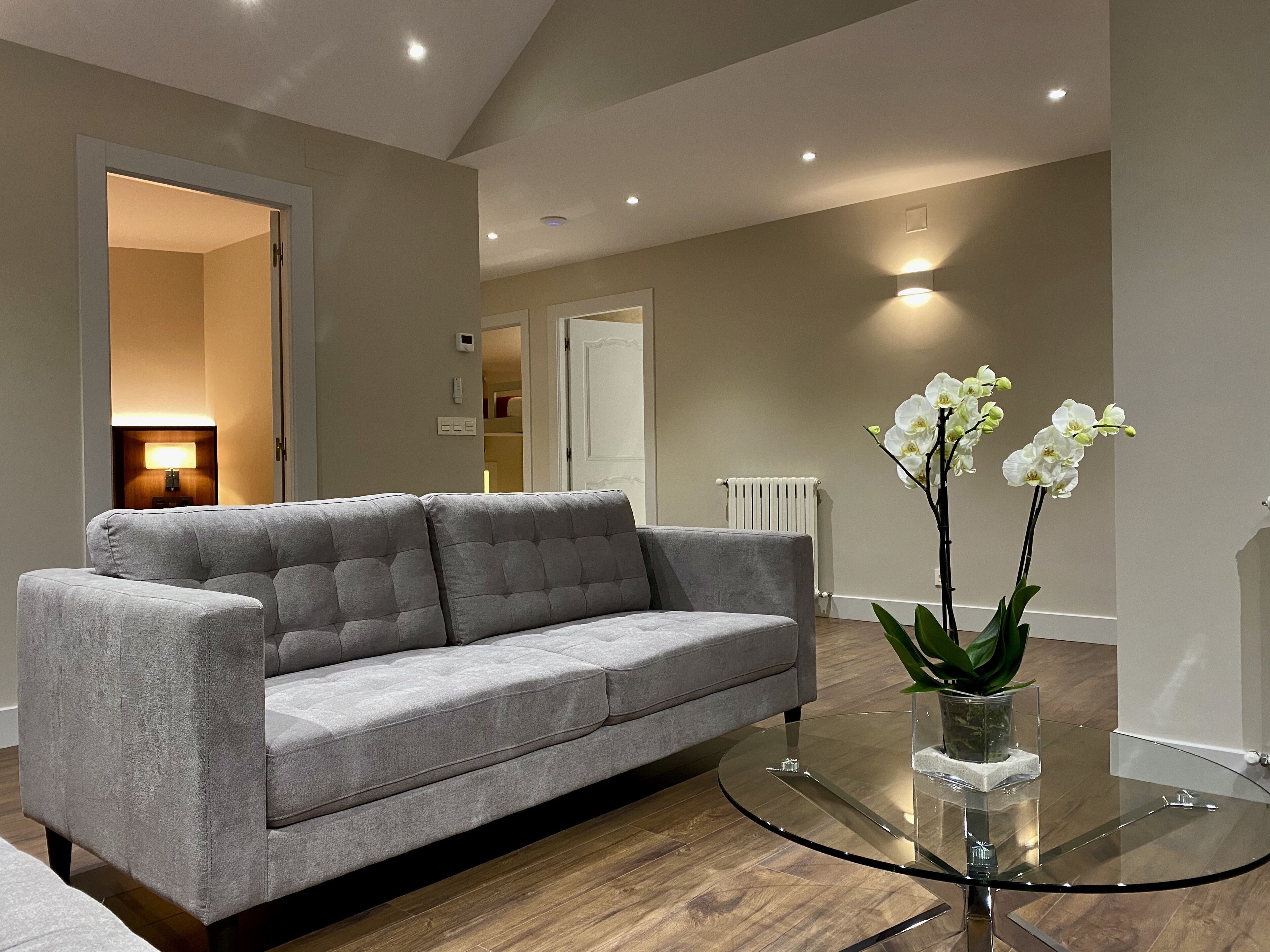 Ein modernes Wohnzimmer mit einem grauen Sofa, einem Glastisch und weißen Orchideen.