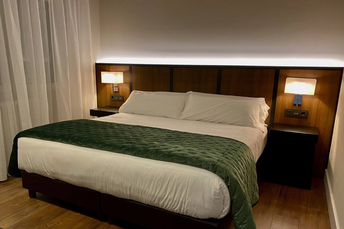 Quarto de hotel com uma cama, duas mesas de cabeceira e uma luminária.