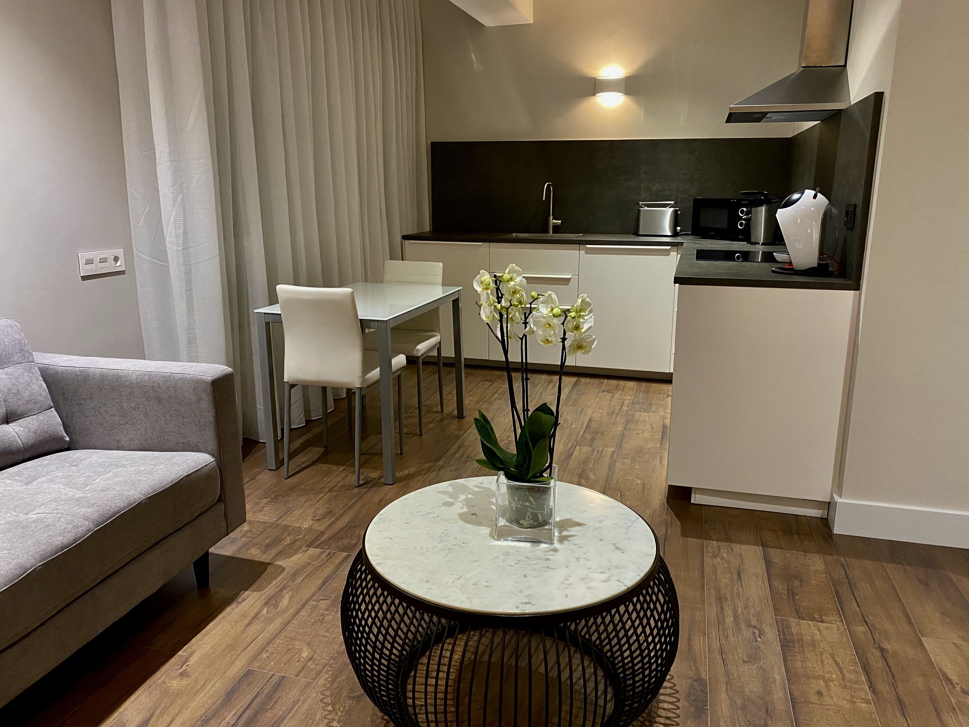 Una sala moderna con un sofá, una mesa de comedor y sillas. Hay una zona de cocina con estufa, microondas y cafetera.