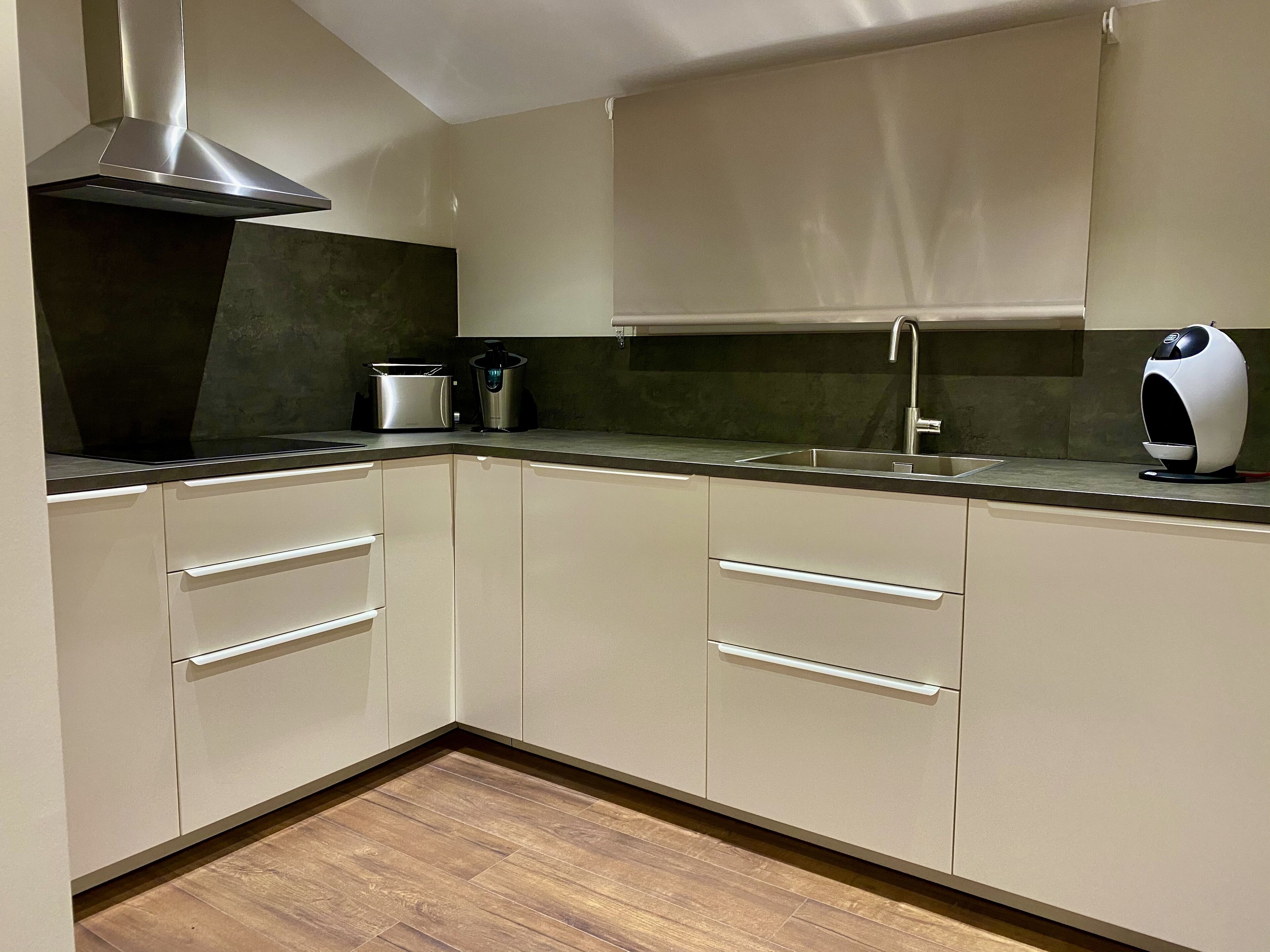 A modern kitchen with white cabinets, a stainless steel range hood, a built-in oven, a sink, and a coffee machine.