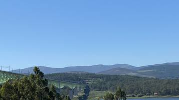A green bridge over a river with forested hills in the background.