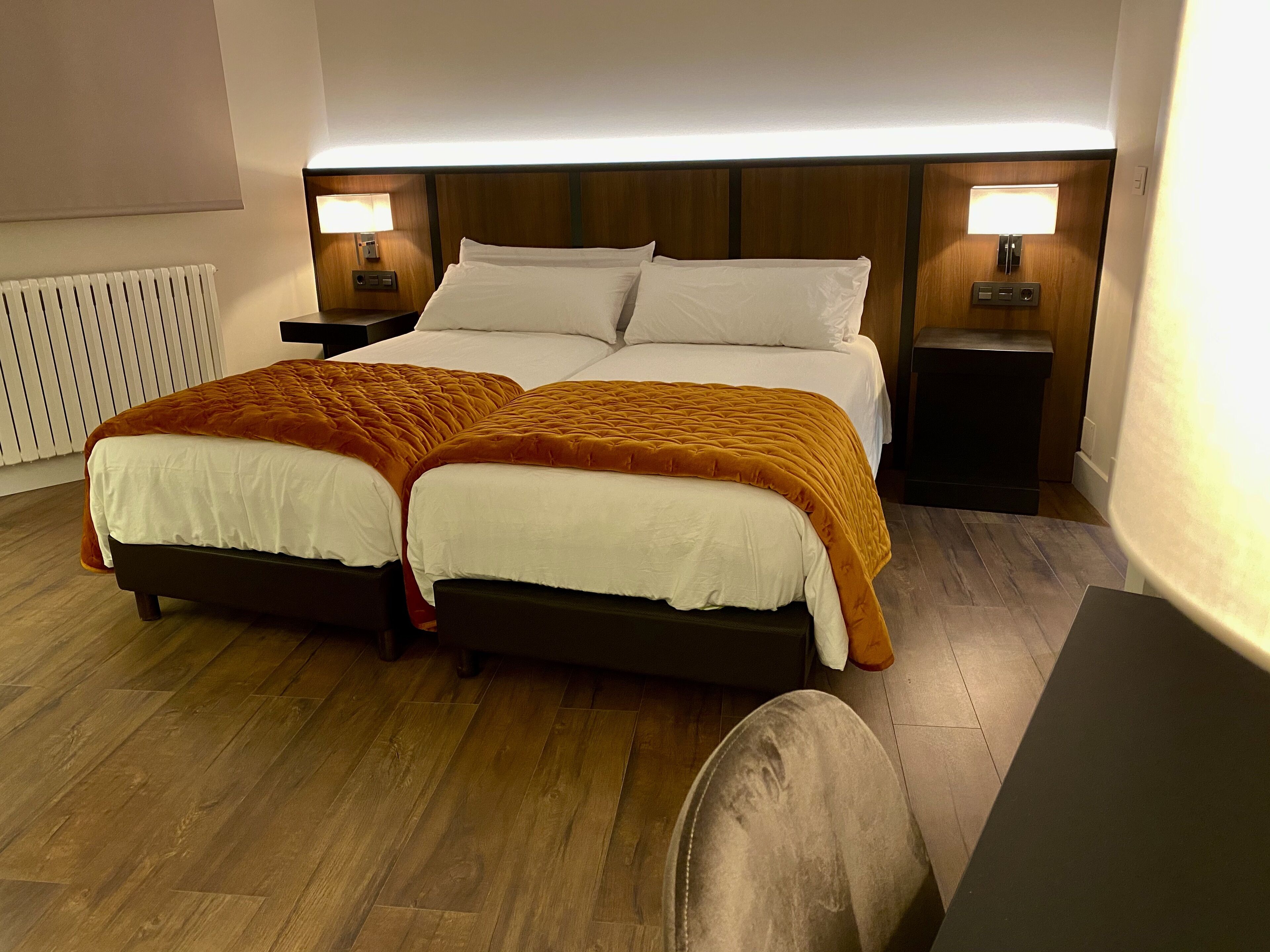 A double bed with a white and orange bedspread, two bedside tables with lamps, and a wooden headboard.