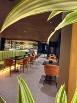 Un restaurante moderno con zona de bar, asientos verdes y sillas anaranjadas.