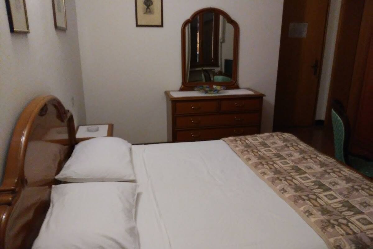A bedroom with a wooden bed, a dresser with drawers, a mirror, and a door.