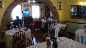 A restaurant with an arched brick entrance, tables set for dining, and a television in the background. - Albergo Ristorante La Campagnola (Urbana)