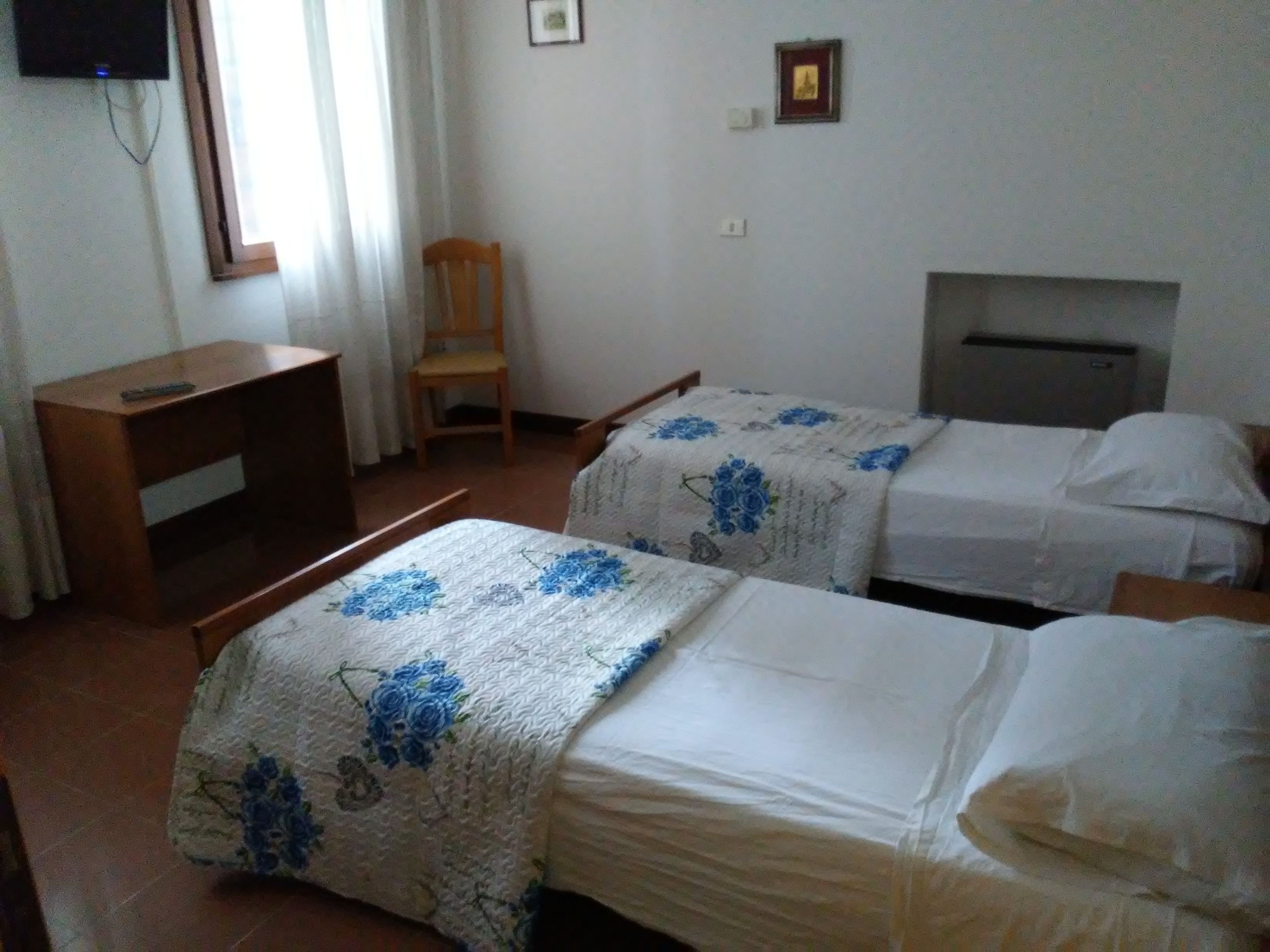 A hotel room with two beds, a desk, a chair, a television, and a fireplace.