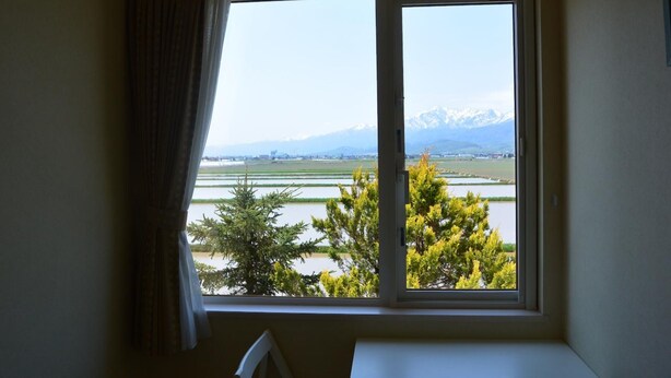 A room with a large window offering a view of a lake, trees, and distant mountains. - Meguminoyu (Furano)